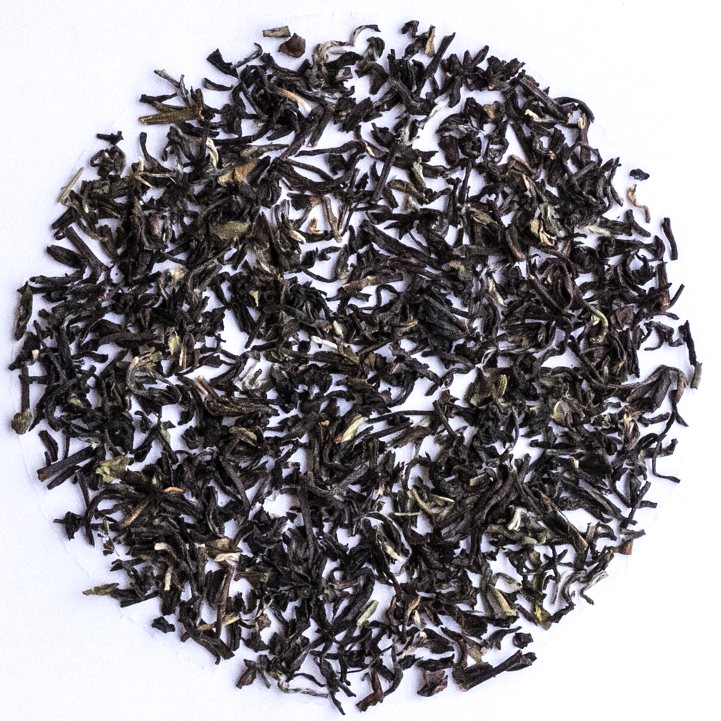 Loose-leaf tea leaves, dark brown to black with subtle green and light brown highlights, arranged in a circular pile on a plain white background.