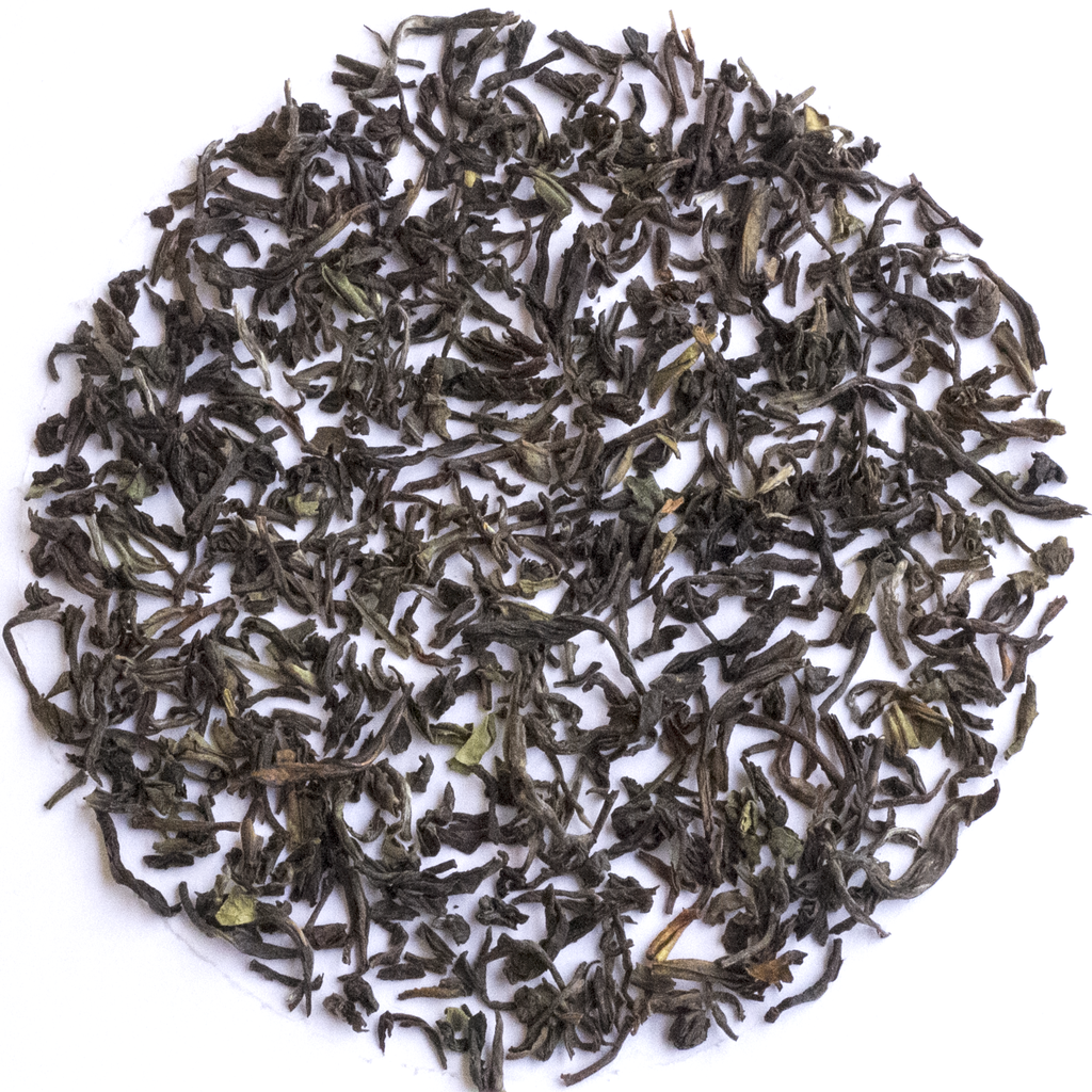 Loose-leaf tea leaves, dark brown and black with small green tips, arranged in a circular pile on a white background.
