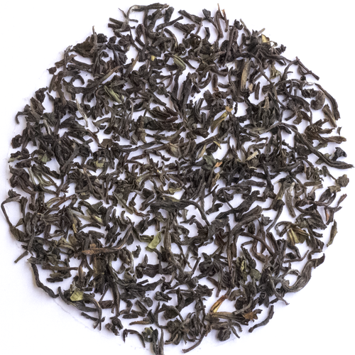 Loose-leaf tea leaves, dark brown and black with small green tips, arranged in a circular pile on a white background.