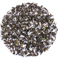 Loose-leaf tea leaves, primarily dark green with some brown and light green accents, arranged in a circular pile on a solid white background.