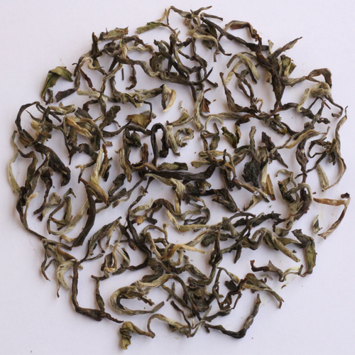 Loose-leaf tea leaves, characterized by their curly, twisted shapes and mix of dark green, olive, and light yellowish-green tones, arranged in a circular pile on a plain white background.