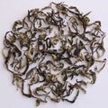 Loose-leaf tea leaves, characterized by their curly, twisted shapes and mix of dark green, olive, and light yellowish-green tones, arranged in a circular pile on a plain white background.