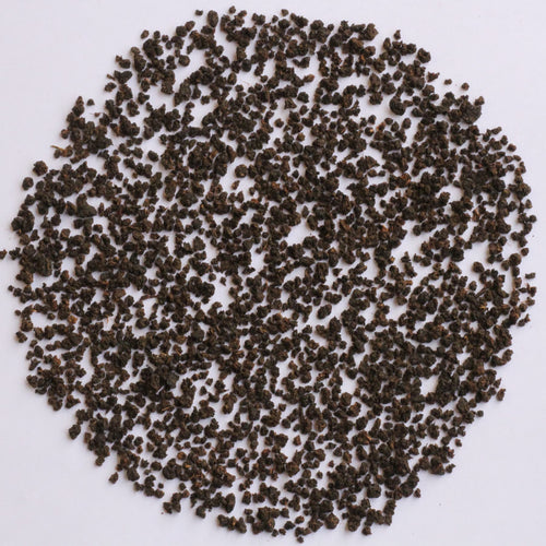 A pile of small dark brown to black granular particles or seeds arranged in a circular shape on a plain white background.