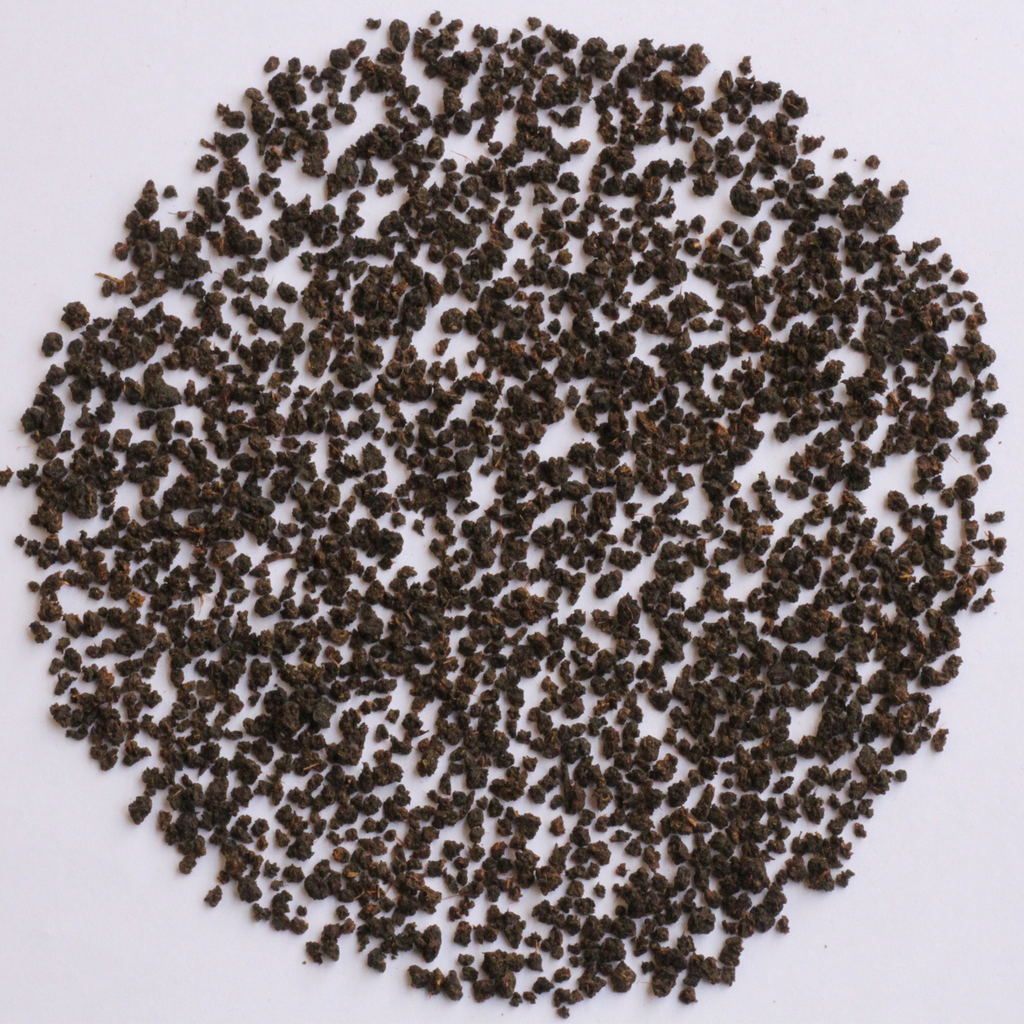 A pile of small dark brown to black granular particles or seeds arranged in a circular shape on a plain white background.