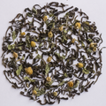 Dried loose-leaf tea with small yellow chamomile flowers scattered in a circular arrangement on a plain white background.