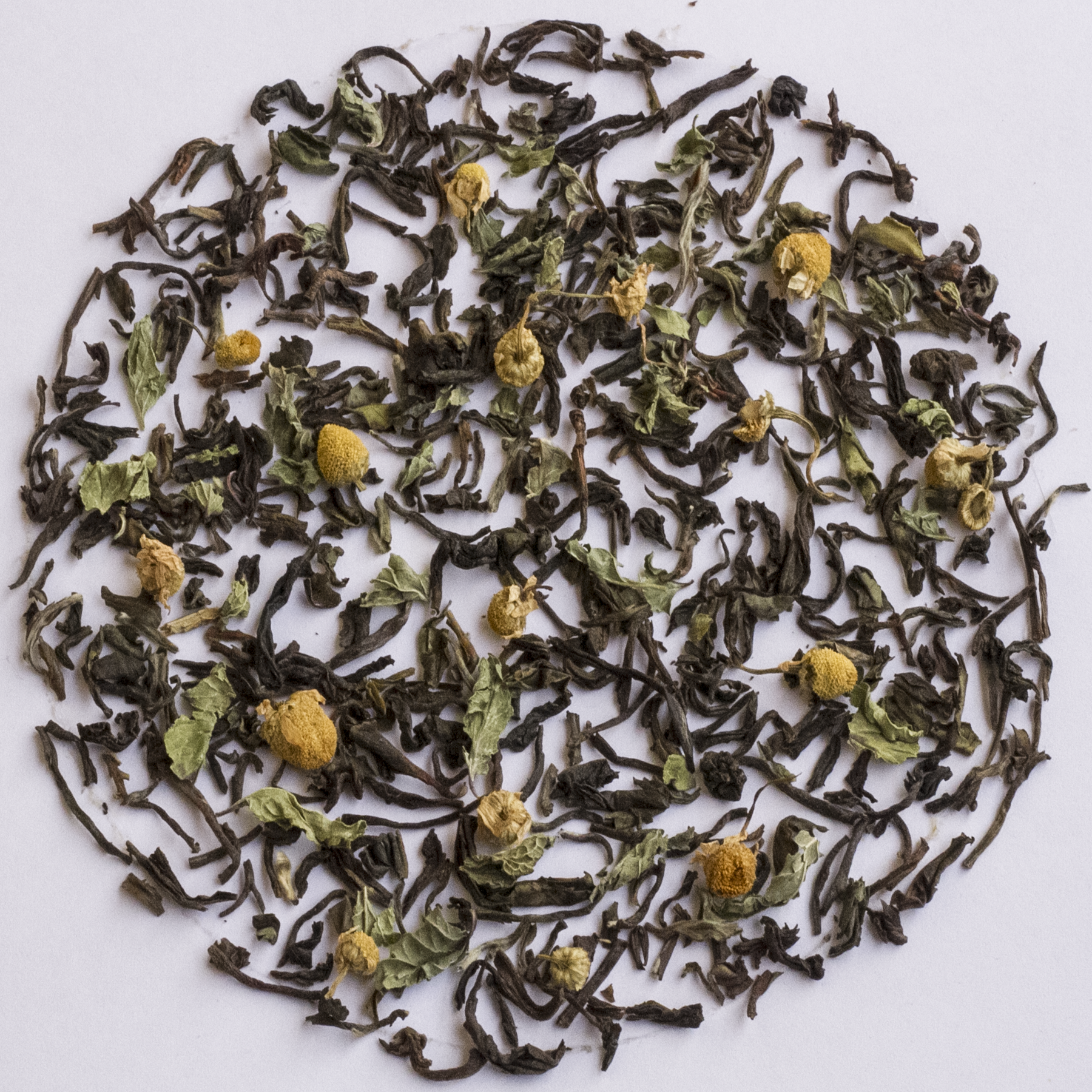 Dried loose-leaf tea with small yellow chamomile flowers scattered in a circular arrangement on a plain white background.