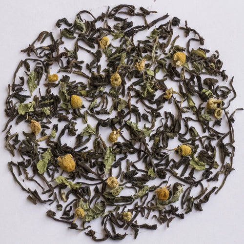 Loose-leaf herbal tea blend featuring dark dried tea leaves and scattered yellow chamomile flowers, arranged in a circular pattern on a white background.