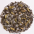 Loose-leaf tea leaves, featuring a mix of dark brown and light olive-green dried leaves, arranged in a circular pattern on a solid white background.