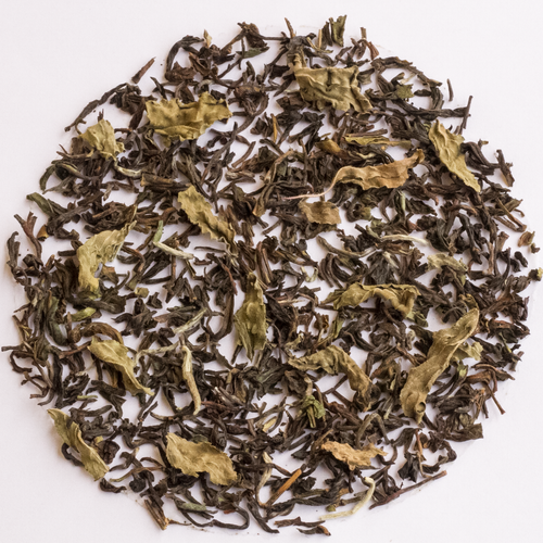 Loose-leaf tea leaves, featuring a mix of dark brown and light olive-green dried leaves, arranged in a circular pattern on a solid white background.