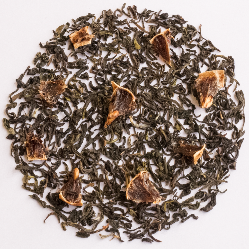 Loose leaf tea arranged in a circular pile on a white background, featuring dark green tea leaves with several dried citrus slice pieces mixed throughout.