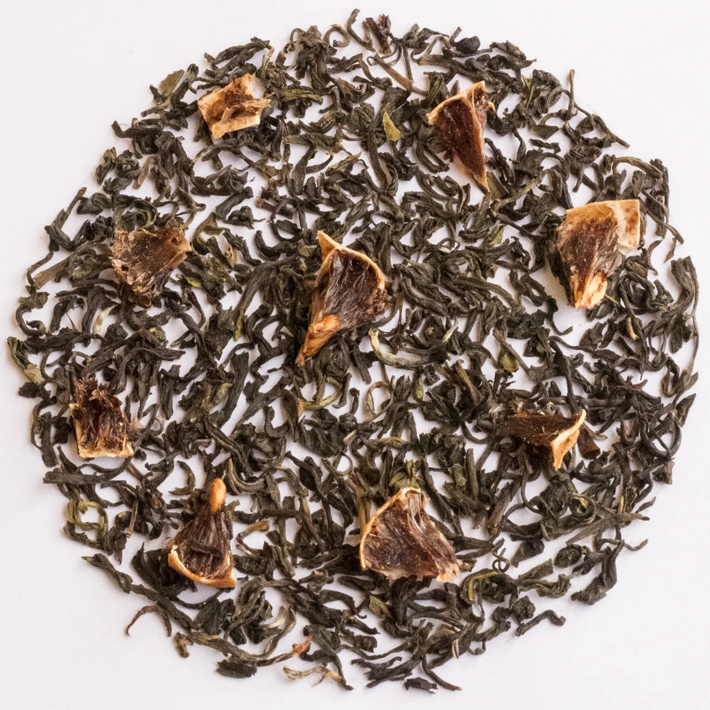 Loose-leaf tea blend with dark green rolled leaves and scattered dried citrus slices, arranged in a circular pile on a white background.