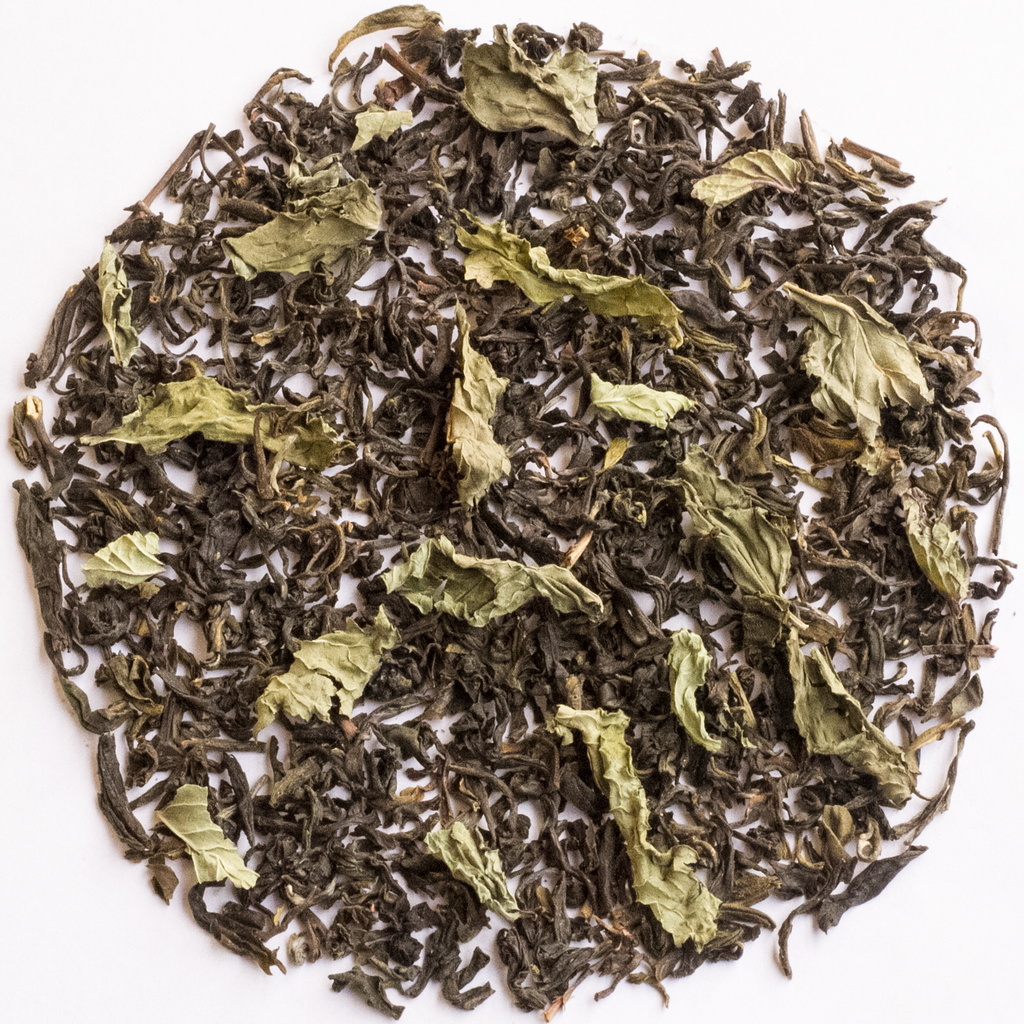 Loose-leaf herbal tea blend with dark brown dried leaves and pale green tea leaves, arranged in a circular pile on a white background.