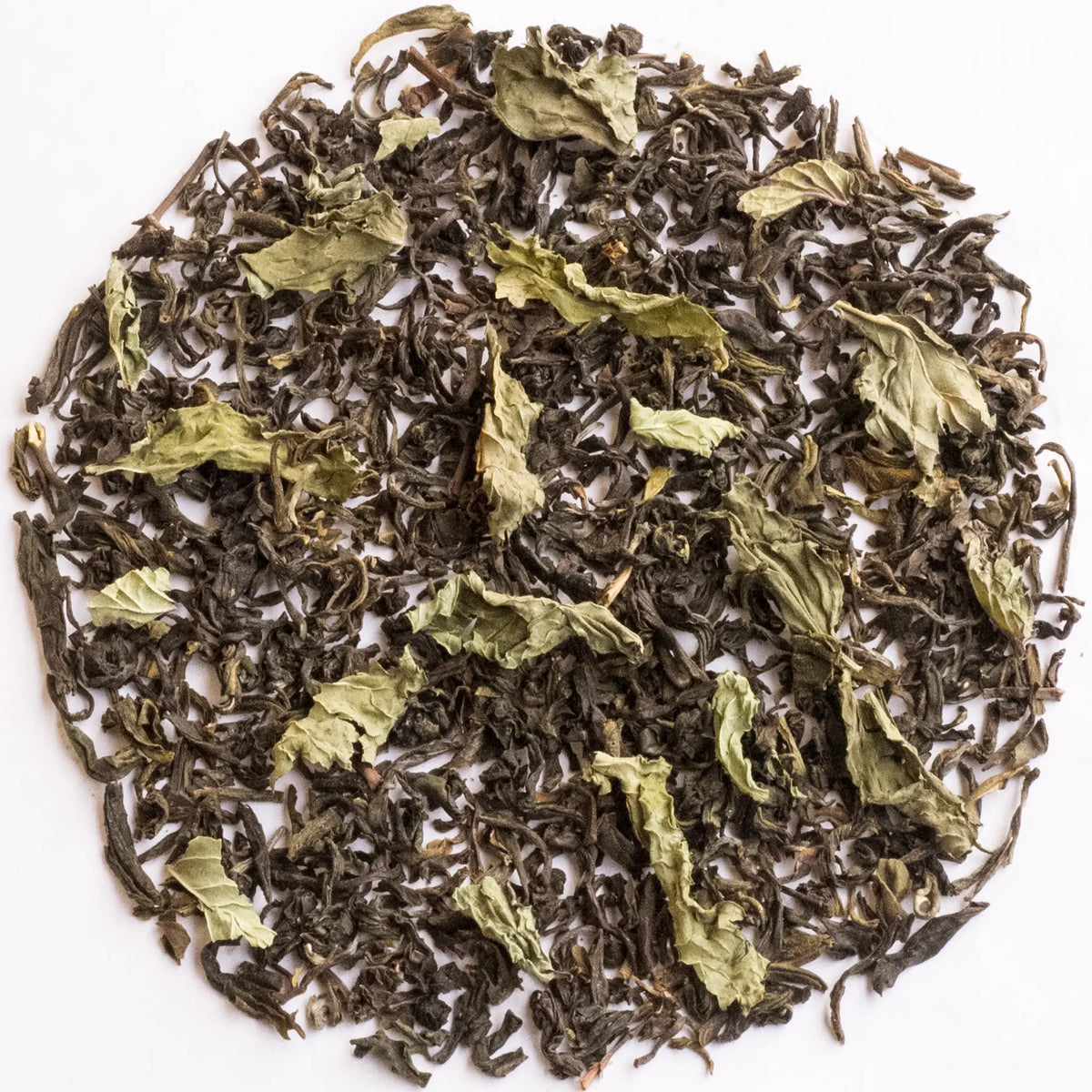 Loose-leaf herbal tea blend with dark brown dried leaves and pale green tea leaves, arranged in a circular pile on a white background.