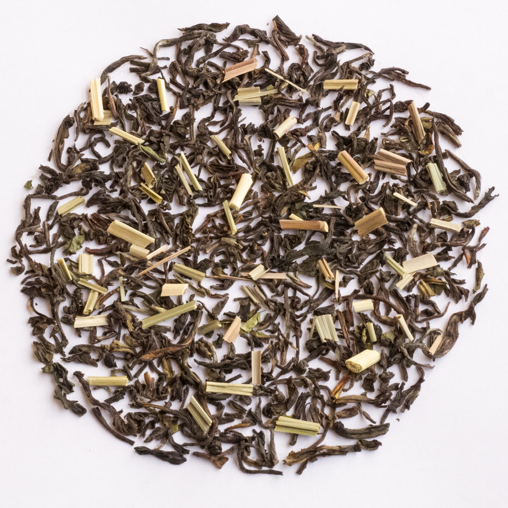 Loose leaf tea scattered in a circular pile on a plain white background, showing dark brown dried leaves mixed with pale yellow-green herb pieces.
