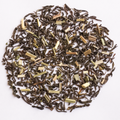 Loose leaf tea scattered in a circular pile on a plain white background, showing dark brown dried leaves mixed with pale yellow-green herb pieces.