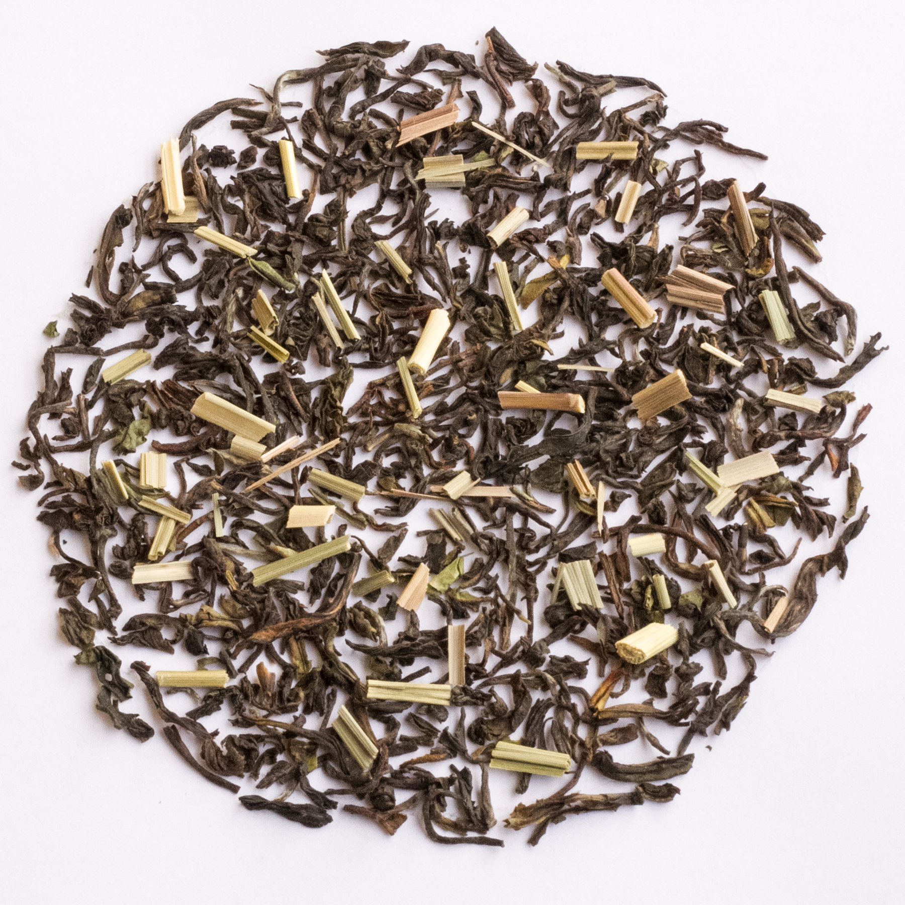 Loose leaf tea scattered in a circular pile on a plain white background, showing dark brown dried leaves mixed with pale yellow-green herb pieces.