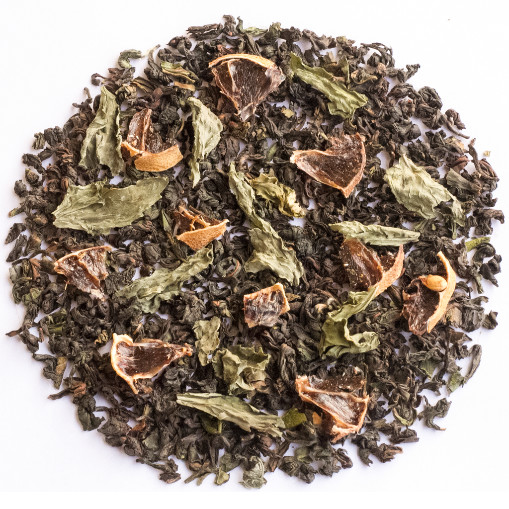 Loose-leaf herbal tea blend featuring dark green tea leaves, dried green citrus peel, and dried orange slices, arranged in a circular pile on a white background.