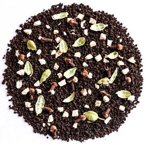 A circular pile of dark brown coffee grounds mixed with whole spices including cardamom pods, cloves, cinnamon sticks, and cubed white sugar, photographed from directly above on a white background.