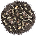 A top-down view of a circular pile of dark brown coffee grounds mixed with dried herbs, leaves, and small brown fruit pieces on a plain white background.