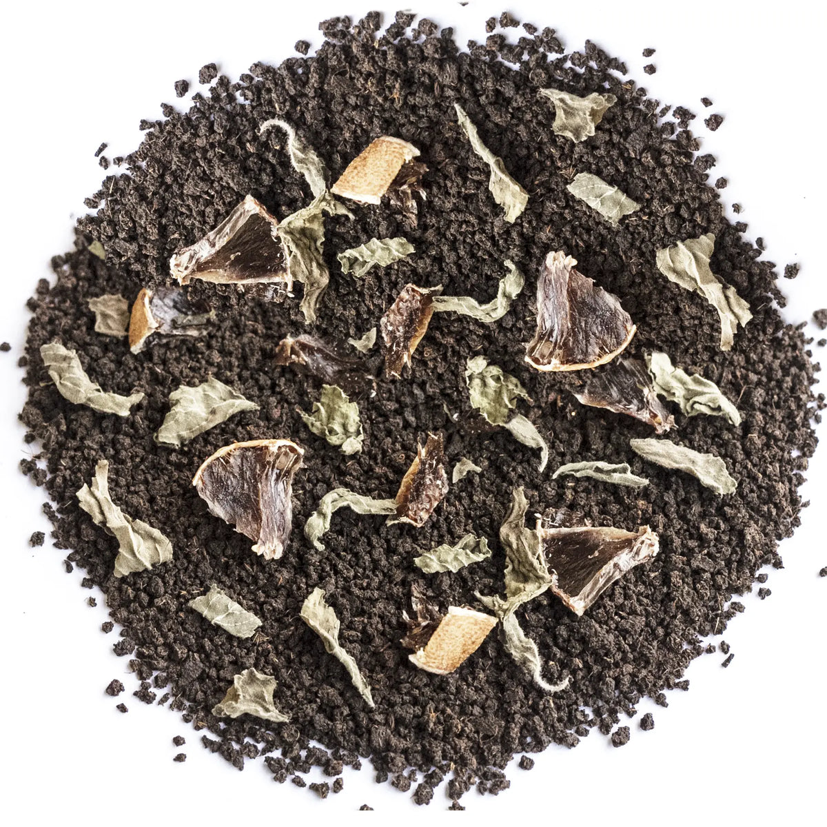A top-down view of a circular pile of dark brown coffee grounds mixed with dried herbs, leaves, and small brown fruit pieces on a plain white background.