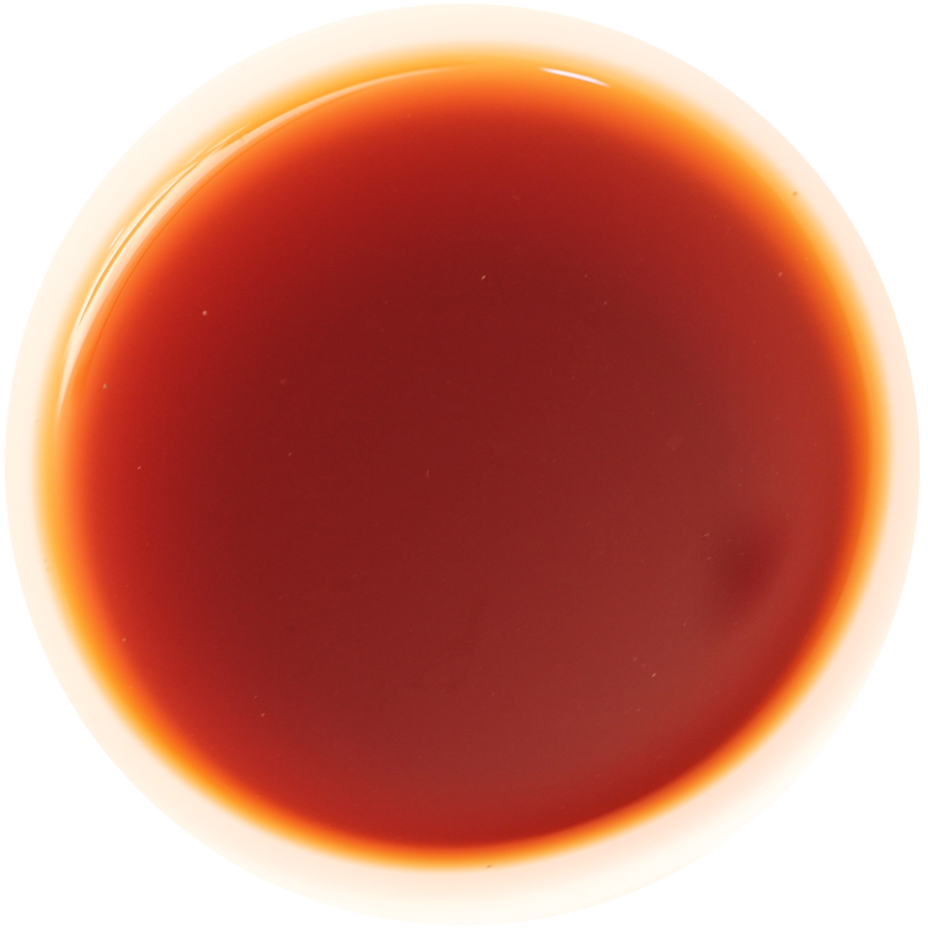 A top-down view of a circular container filled with a deep reddish-brown liquid, likely a sauce, syrup, or oil, on a solid white background.