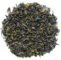 A pile of loose-leaf tea leaves, showing dark green to black rolled leaves with bright yellow-green tips, photographed on a plain white background.