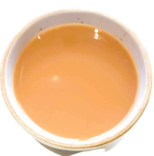 A top-down view of a light brown liquid, likely milk tea or coffee with milk, served in a white ceramic cup against a white background.