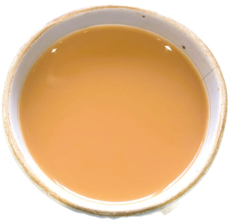 A top-down view of a light brown liquid, likely coffee or tea, served in a white ceramic bowl with a rustic beige rim, set against a plain white background.