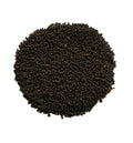A circular pile of small dark brown to black seeds or grains on a plain white background.