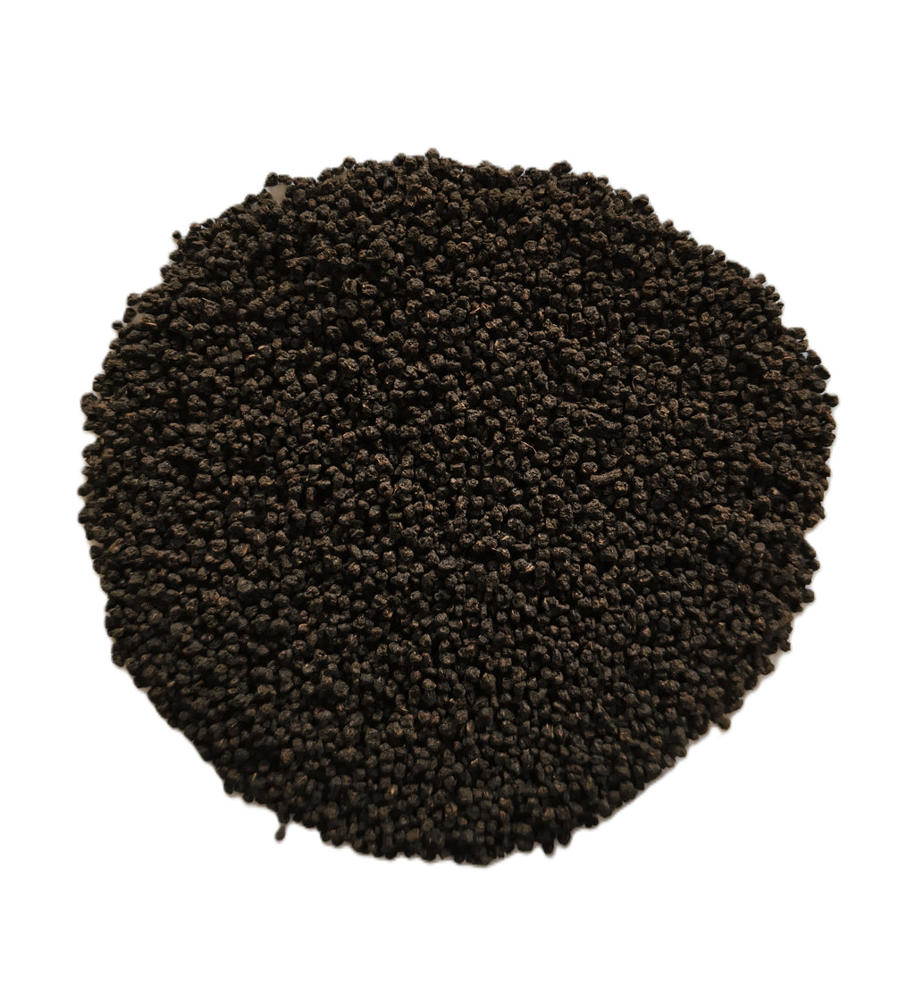 A pile of small dark brown to black granular particles, likely seed, soil, or coffee beans, arranged in a circular mound on a solid white background.