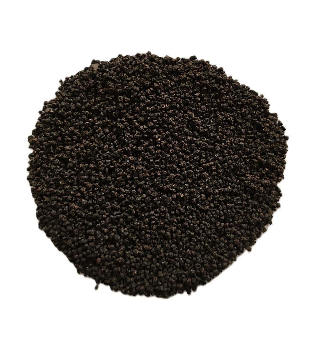 A pile of small dark brown to black granular particles, likely seed, soil, or coffee beans, arranged in a circular mound on a solid white background.