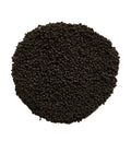 A pile of small dark brown to black granular particles, likely seed, soil, or coffee beans, arranged in a circular mound on a solid white background.