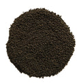 A circular pile of dark brown to black granular material, likely coffee grounds or seed pods, photographed from directly above on a solid white background.