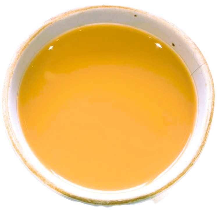 A top-down view of a shallow white ceramic bowl filled with a smooth, glossy golden yellow liquid, set against a plain white background.