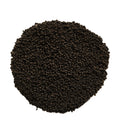 A pile of small dark brown to black granular particles, likely seed, soil, or coffee beans, arranged in a circular mound on a solid white background.