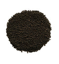 A circular pile of small dark brown to black seeds or grains on a plain white background.