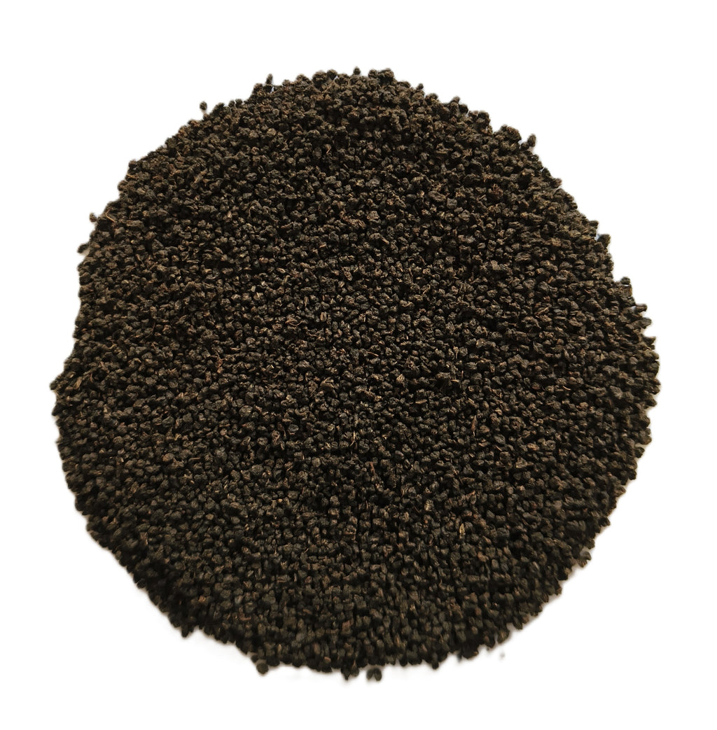 A circular pile of dark brown to black granular material, likely coffee grounds or seed pods, photographed from directly above on a solid white background.