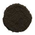 A circular pile of dark brown to black granular material, likely coffee grounds or seed pods, photographed from directly above on a solid white background.