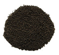 A pile of small dark brown to black seeds or grains photographed from above on a plain white background.