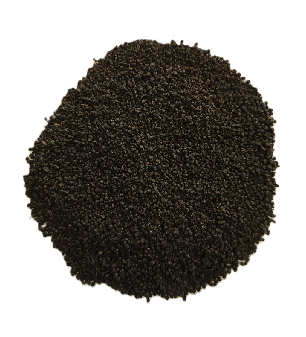 A pile of dark brown to black granular material, likely coffee grounds or seed pods, photographed from directly above on a solid white background.
