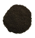 A pile of dark brown to black granular material, likely coffee grounds or seed pods, photographed from directly above on a solid white background.