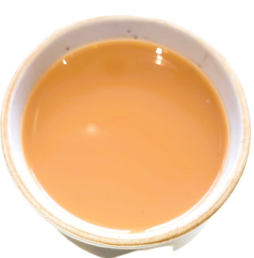 A top-down view of a light brown liquid, likely milk tea or coffee with milk, served in a white ceramic cup against a white background.