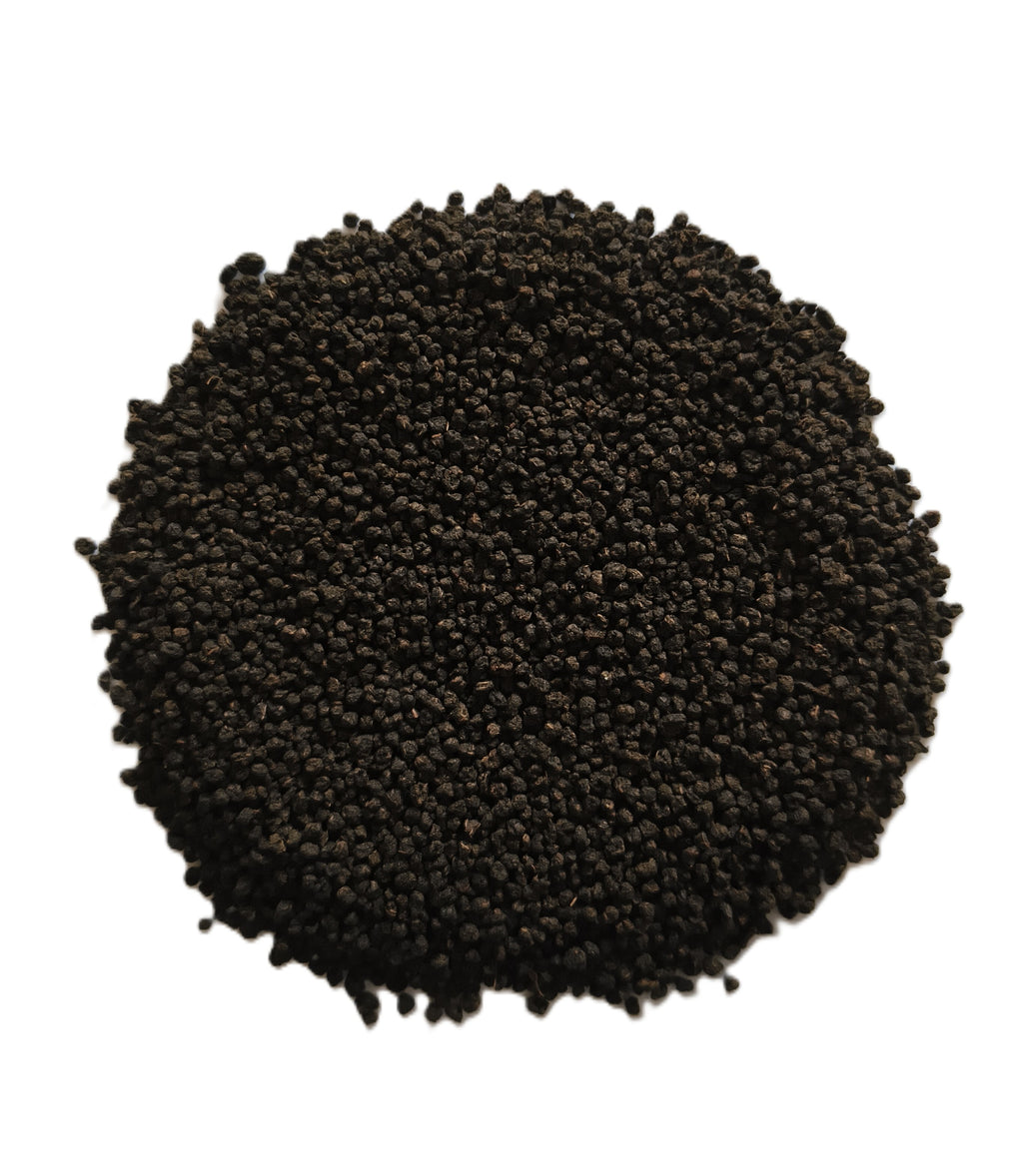 A pile of small dark brown to black granular seeds or pellets, photographed from above on a plain white background.