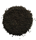 A pile of small dark brown to black seeds or granules photographed from above on a plain white background.