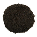 A pile of dark brown to black textured seeds or granules, photographed from directly above on a plain white background.