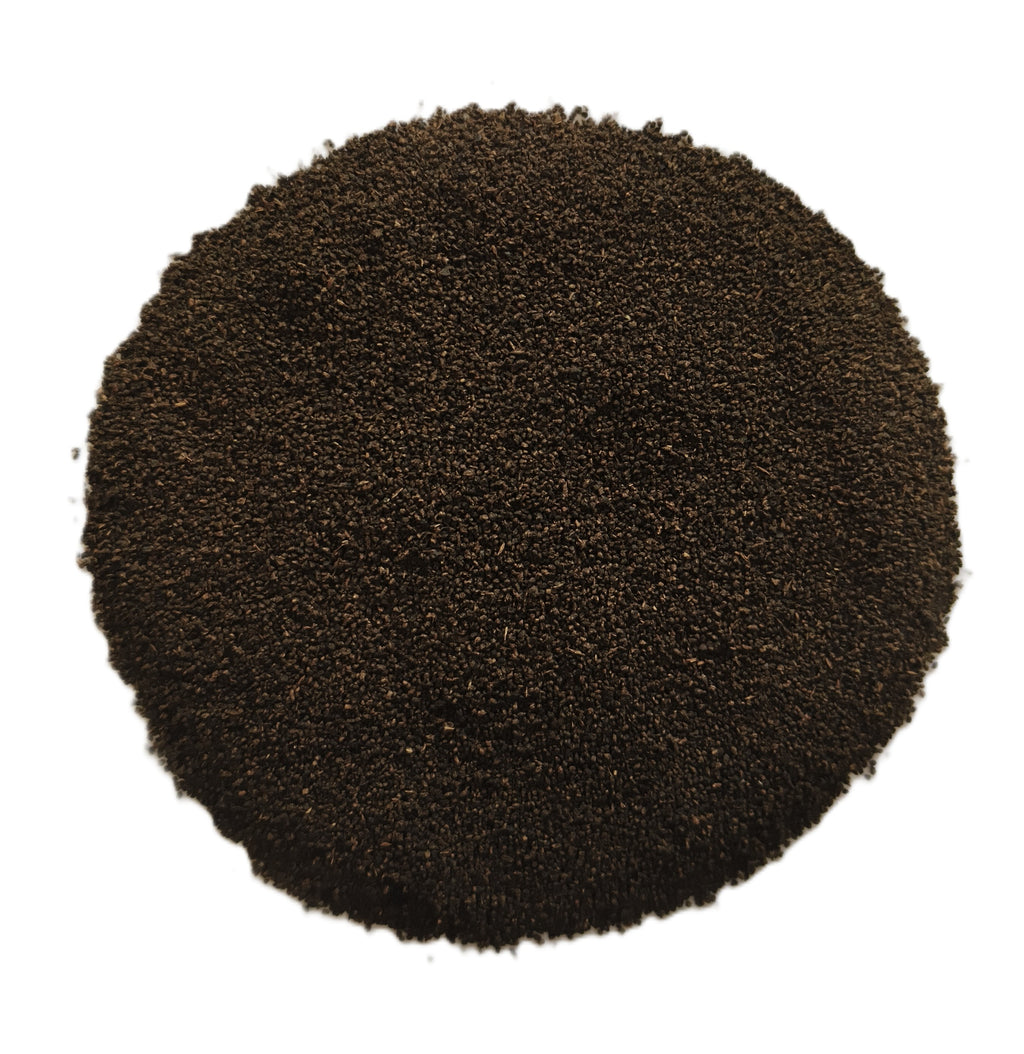 A circular pile of dark brown granular material, likely coffee grounds or seed kernels, photographed from directly above on a solid white background.