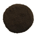 A circular pile of dark brown granular material, likely coffee grounds or seed kernels, photographed from directly above on a solid white background.