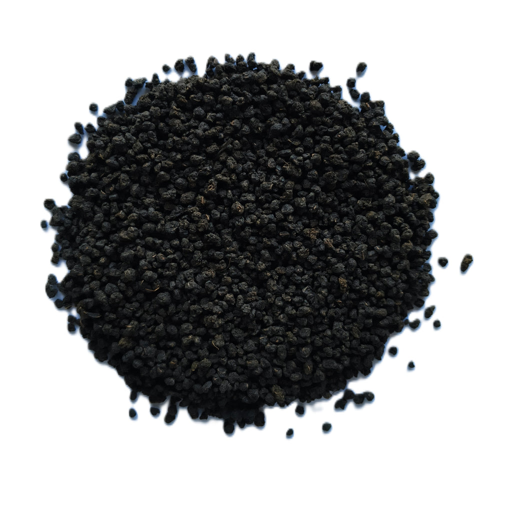 A pile of small, dark brown to black dried seeds or granules, photographed from directly above on a solid white background.
