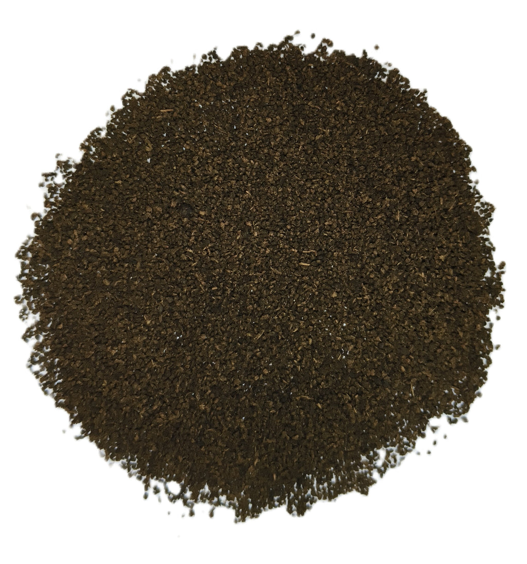 A circular pile of dark brown, finely ground granular material, likely coffee beans or tea leaves, photographed from directly above on a solid white background.