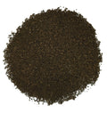 A circular pile of dark brown, finely ground granular material, likely coffee beans or tea leaves, photographed from directly above on a solid white background.